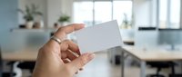 Hand holding blank white business card in modern office workspace for corporate branding and professional networking mockup template design.