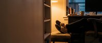 Man in casual attire relaxing with feet up on desk in modern office workspace during evening hours, suitable for corporate lifestyle and work-life balance concepts.