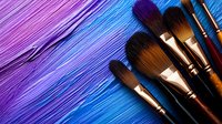 Professional makeup brushes arranged on vibrant purple and blue textured background with diagonal composition, creating artistic contrast between tools and colors.