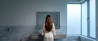 Modern minimalist bathroom with young woman in white robe standing at marble vanity, natural light from large window, contemporary interior design for luxury home.