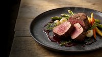Sliced medium-rare beef tenderloin with asparagus and colorful vegetables on dark plate, gourmet restaurant presentation for fine dining menu.