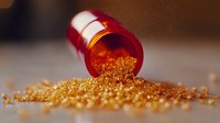 Orange prescription bottle spilling golden medicine granules on surface, macro pharmaceutical photography showing detailed medical crystals in warm lighting.