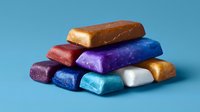 Colorful metallic clay bars stacked in pyramid formation against blue background, showing texture and shine of polymer material. Artistic craft supplies.
