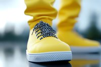 Yellow casual sneaker with checkered laces against blurred background, close-up view showing modern urban footwear style and distinctive design details.