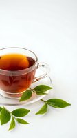 Glass cup of hot black tea with fresh green tea leaves on white background isolated for beverage and wellness design projects.