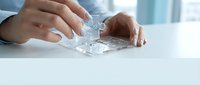 Businessman hands assembling white jigsaw puzzle pieces on desk in modern office environment representing teamwork and problem solving strategies.