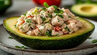 Fresh tuna salad with diced vegetables and herbs served in halved avocado bowl, healthy protein-rich meal ready for lunch or dinner preparation.