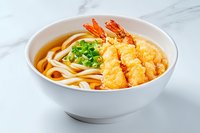 Crispy tempura shrimp udon noodle soup in white ceramic bowl with green onions and clear broth on marble surface, traditional Japanese cuisine.
