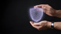 Male hands holding glowing digital shield icon with wireframe design on dark background, representing cybersecurity, data protection, and network safety for technology concepts.