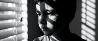 Young Asian woman in dramatic black and white portrait with venetian blind shadows creating striking light patterns across her face and body.