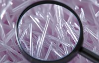 Magnifying glass examining crystalline structures on pink background, showing scientific research and molecular analysis in close-up macro photography.