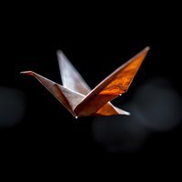 Glowing orange origami crane in flight against dark background, illuminated paper art casting dramatic shadows and highlights, artistic Japanese folded creation.