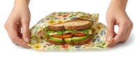 Fresh sandwich with vegetables and greens wrapped in eco-friendly paper, held by hands on white background. Sustainable food packaging concept.