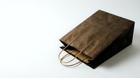 Brown paper shopping bag with handles lying on white background for retail packaging and eco-friendly commerce applications.
