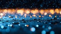 Magical glowing bokeh lights on dark blue glittery surface create dreamy abstract background with orange and blue sparkles for festive holiday designs.