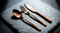 Copper flatware set with fork, knife, and spoon arranged on textured slate surface for dining and tableware design projects.