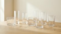 Collection of empty clear glass drinkware on wooden surface against neutral beige wall background for kitchen and dining room interior design concepts.