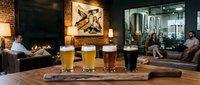 Craft beer tasting flight with four glasses of different beer styles displayed on wooden counter in modern brewery taproom with brick walls and industrial decor.