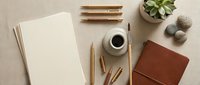 Minimalist workspace with blank paper, coffee cup, wooden pencils, leather notebook and succulent plant on neutral linen background for creative projects.