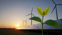 Green plant seedling growing in front of wind turbines and solar panels at sunset representing renewable energy and sustainable development.