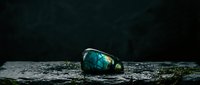 Iridescent labradorite gemstone with blue and green flash on textured stone surface against dark background for jewelry and mineral collection displays.