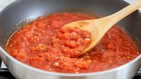 Fresh tomato sauce simmering in non-stick pan with wooden spoon, chunky texture and vibrant red color shows homemade cooking process in kitchen.