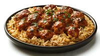 Glazed chicken meatballs served on bed of seasoned rice in black ceramic plate, garnished with fresh herbs and savory sauce, restaurant quality meal.