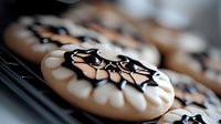 Chocolate glazed cookies with elegant black and white swirl pattern decoration on cooling rack, fresh baked homemade dessert treats.