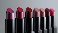 Row of luxurious lipsticks in various shades of red and pink arranged in gradient order against dark background, showcasing modern cosmetic products in elegant packaging.