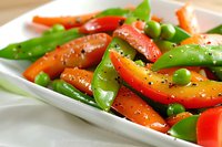 Fresh stir-fried vegetables with snow peas, red bell peppers, carrots and green peas seasoned with black pepper served on white ceramic plate.