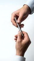 Two male hands passing a silver metallic pen on a white background, symbolizing agreement, signing a contract, or business deal.