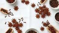 Aromatic star anise and cloves scattered with wooden scoops on white background. Warm spices for cooking, baking and seasonal recipes.