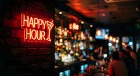 Red neon happy hour sign glowing on brick wall in dimly lit bar with blurred background of bottles and warm atmospheric lighting for nightlife concept.