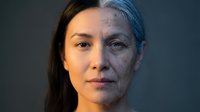 Young woman face showing aging process transformation from youth to elderly with wrinkles and gray hair against dark background for skincare concepts.