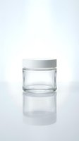 Empty glass cosmetic jar with white lid on reflective surface for skincare and beauty product packaging.