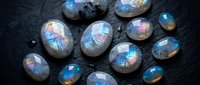 Collection of iridescent labradorite gemstones with rainbow flash effects on dark textured surface for jewelry making and crystal healing practices.