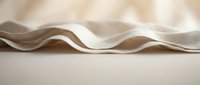 Folded beige and white fabric with soft waves and natural texture, suitable for textile design, fashion backgrounds, and material mockups.