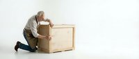 Senior Caucasian man in casual clothing kneeling while unpacking large cardboard box on white background, moving day concept for relocation services.