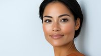 Young Asian woman with natural makeup and glowing skin smiling confidently against light background, wellness and beauty concept for cosmetic advertising.