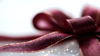 Elegant burgundy velvet ribbon bow with golden edge against blurred bokeh background, macro shot showing luxurious textile texture and festive sparkle.