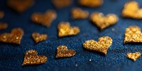 Golden glitter heart shapes scattered on dark blue textured background, creating romantic festive decoration for Valentine's Day or wedding celebrations.