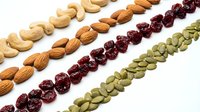 Healthy mixed nuts and dried fruits arranged in diagonal rows on white background. Cashews, almonds, cranberries, pumpkin seeds for snacking and cooking.