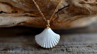 White shell pendant necklace on gold chain displayed against weathered driftwood. Coastal jewelry accessory for beach lovers and ocean-inspired fashion.