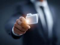 Businessman in dark suit pointing at glowing digital folder icon floating in air, representing digital document management and cloud storage solutions.