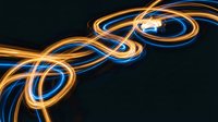 Abstract flowing light trails in blue and orange creating dynamic spiral patterns on dark background for modern digital design projects.
