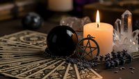 Mystical fortune telling setup with tarot cards, crystal ball, pentagram pendant, burning candle and quartz crystal for divination and spiritual guidance sessions.