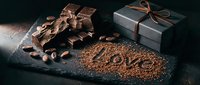 Dark chocolate pieces with cocoa beans, love written in cocoa powder, and a gift box on slate board, perfect for Valentine's Day and holidays.