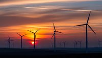 Wind turbines silhouetted against dramatic sunset sky with orange and purple clouds. Renewable energy farm generating clean electricity at dusk.