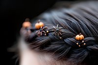 Halloween-themed hair accessories with miniature black spiders and orange pumpkins woven into dark braided hair, creating spooky seasonal style.