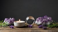 Spiritual wellness setup with amethyst crystals, burning candle, crystal ball and lavender herbs on rustic wooden surface for meditation and healing practices.